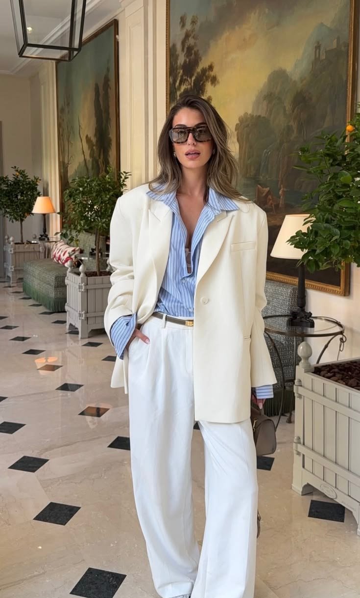Mujer con outfit elegante minimalista usando blazer blanco oversize, pantalón sastre blanco y camisa azul, en el interior de un hotel de lujo